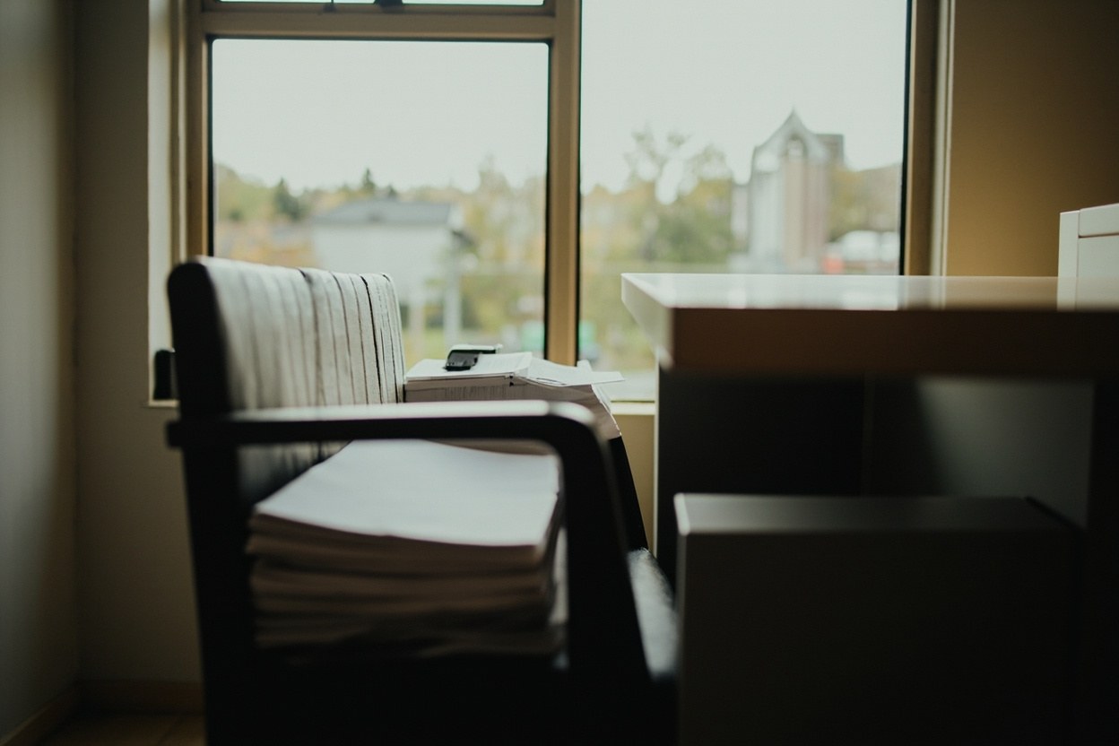 An empty break room with a stack of printed letters on a chair by the window in afternoon daylight
